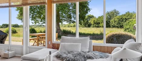 Una sala de estar moderna con un sofá, una mesa de centro y vistas a un jardín a través de amplios ventanales.