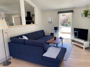 Ein modernes Wohnzimmer mit einem blauen Sofa, einem Couchtisch, einem Fernseher und einem großen Fenster.