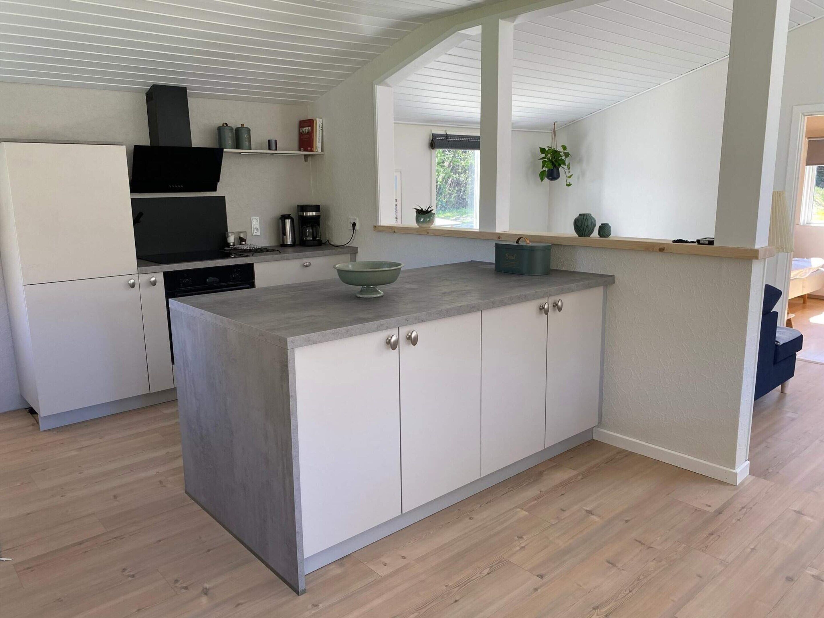 A modern kitchen with a central island, white cabinetry, and a wooden floor.