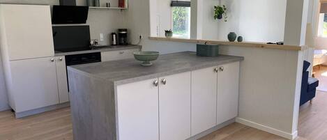 A modern kitchen with a central island, white cabinetry, and a wooden floor.