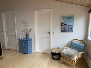 Ein Zimmer mit einem blauen Schrank, einem Korbstuhl mit Felldecke und einem Bild an der Wand.