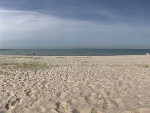 Ein sandiger Strand mit Fußabdrücken und freiem Blick auf das Meer.