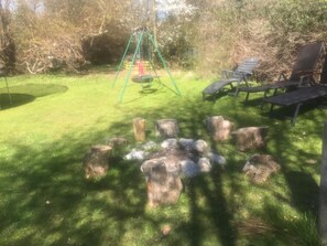 A grassy outdoor area with a swing set, picnic tables, and a fire pit surrounded by tree stumps. - 5 Star Holiday Home in Nykobing Sj (Nykobing Sjaelland)