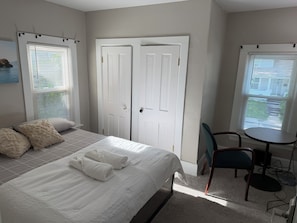 A bedroom with a bed, two doors, a chair, and a small table.