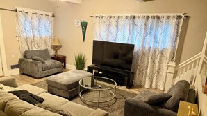 Ein Wohnzimmer mit einer Sofagarnitur, einem Couchtisch, einem Fernseher und Vorhängen.