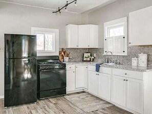 A kitchen with white cabinets, a black refrigerator, a stove, and a window. - Cozy Home close to Notre Dame & Downtown Southbend (South Bend)
