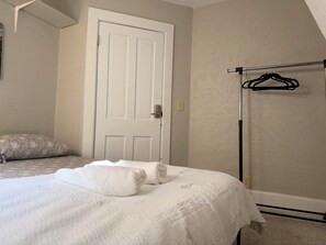Un dormitorio con una cama, una puerta, un perchero con colgadores y una almohada.