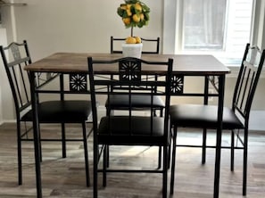 Ett matbord med fyra svarta stolar, en vit vas med gula blommor och ett fönster i bakgrunden.