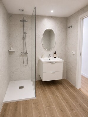 A modern bathroom with a walk-in shower, a vanity with a mirror, and a wooden floor. - El Paraíso Apartment - Downtown Marbella - Free Parking (Marbella)
