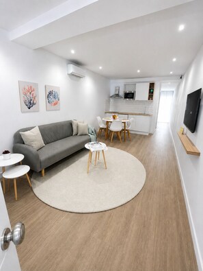 A modern living room with a grey sofa, a round coffee table, and a dining area with white chairs. - El Paraíso Apartment - Downtown Marbella - Free Parking (Marbella)