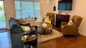Ein Wohnzimmer mit Sofa, Sesseln, Couchtisch, Kamin und einem an der Wand montierten Fernseher.