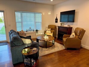 Ein Wohnzimmer mit Sofa, Sesseln, Couchtisch, Kamin und einem an der Wand montierten Fernseher.