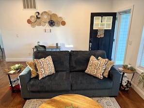 A living room with a dark grey sofa, patterned cushions, a wooden coffee table, and a wall-mounted decorative piece. - Modern 3 BR, 2.5 Bath Townhome / Sleeps 8 / Ideal for work or vacation! (Rockville)
