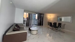 A modern living room with a sofa, a coffee table, and a dining area with chairs and a table. - Brickell Penthouse Breathtaking Views (Miami)