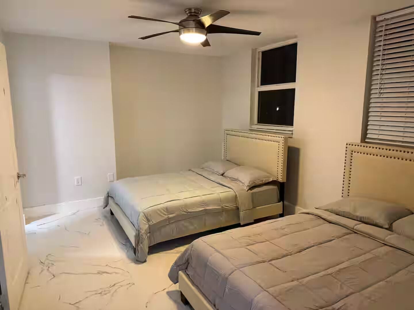 Una camera da letto con due letti, una ventola a soffitto, una finestra con persiane e una porta.