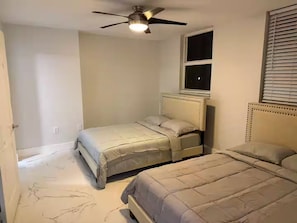 A bedroom with two beds, a ceiling fan, a window with blinds, and a door. - Brickell Penthouse Breathtaking Views (Miami)