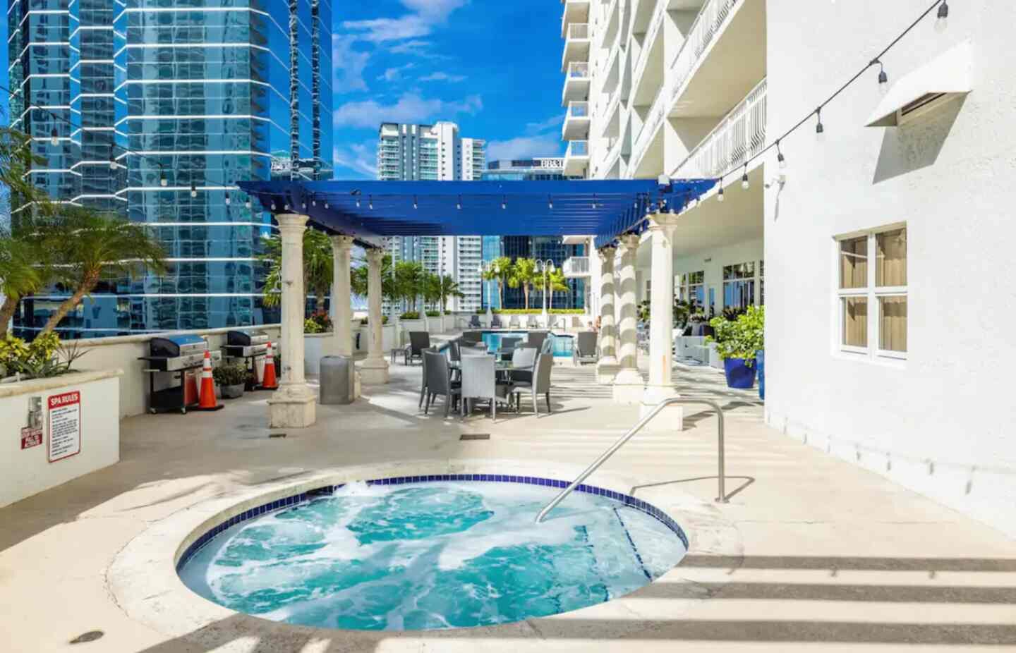 A rooftop pool area with a hot tub, outdoor seating, and a view of surrounding high-rise buildings.