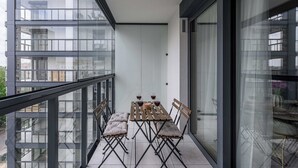 A balcony with a table and chairs, a view of the cityscape, and a glass door. - New House With Pool Near Beach (Warsaw)