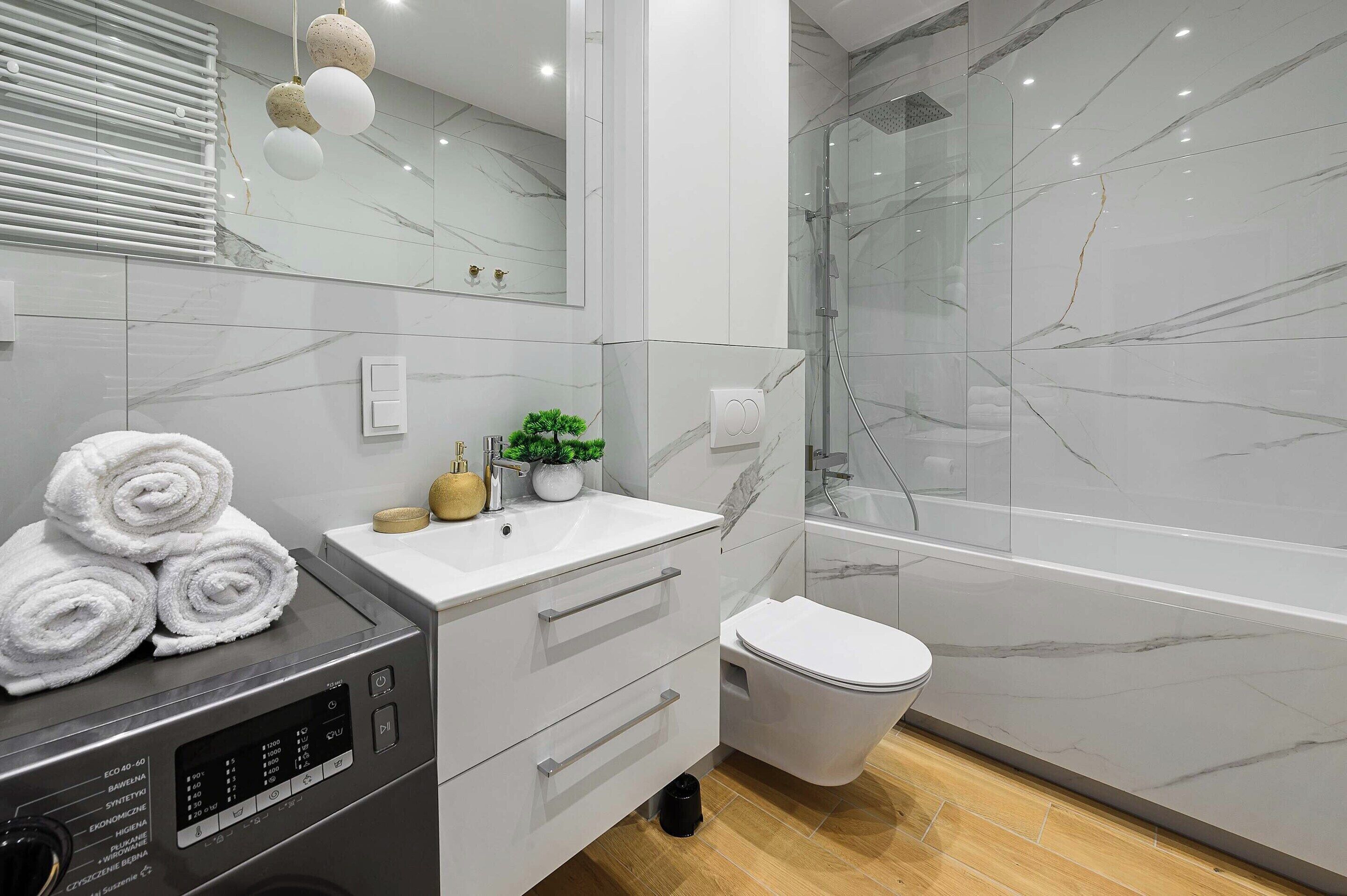Un baño moderno con piso de mármol, cabina de ducha de vidrio, lavamanos blanco y un inodoro.