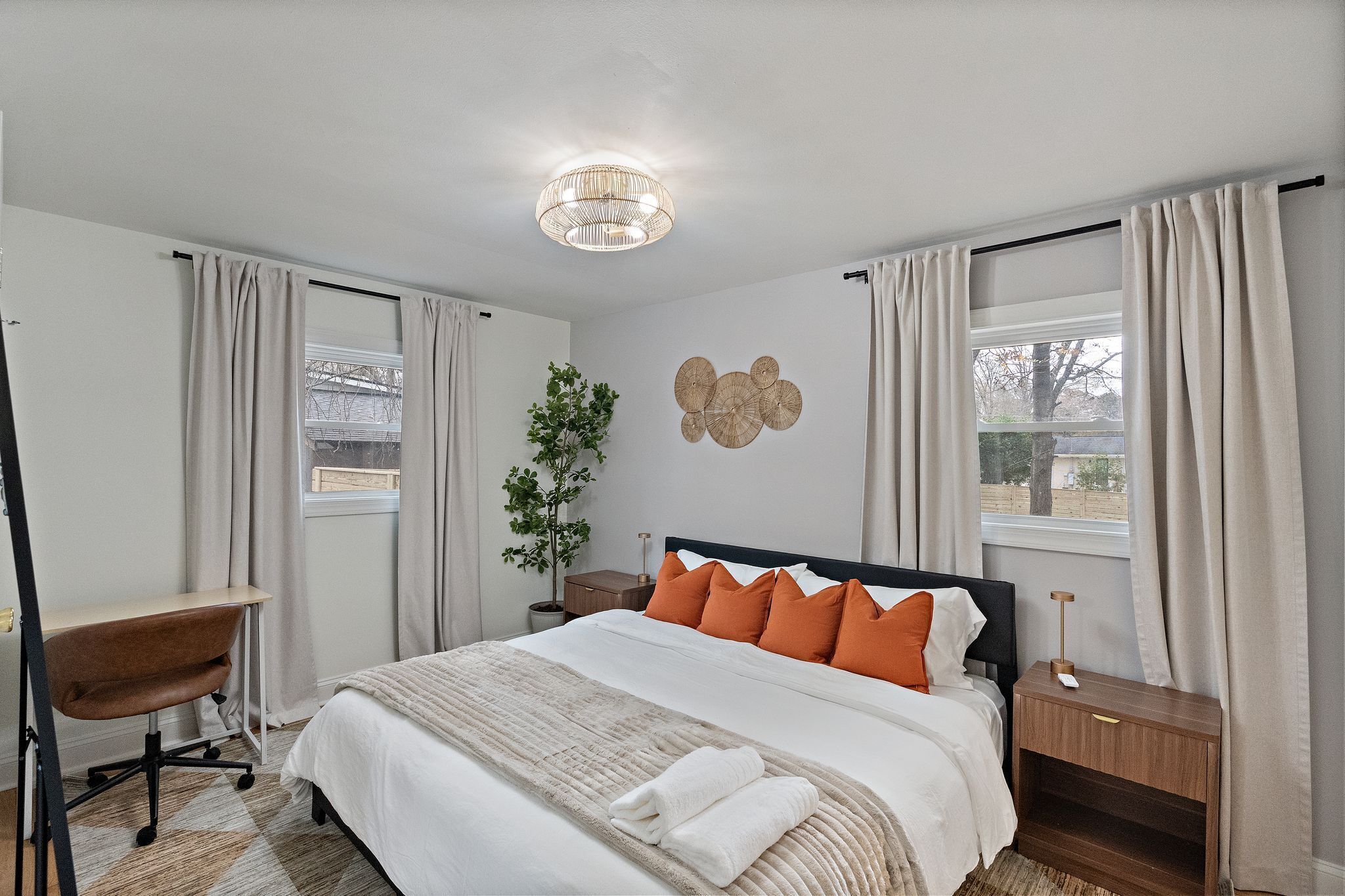 Une chambre à coucher comprenant un lit, un bureau, une chaise, une table de chevet, une lampe et un luminaire fixé au mur.