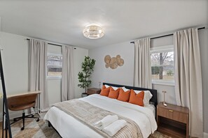A bedroom with a bed, a desk, a chair, a bedside table, a lamp, and a wall-mounted light fixture. - Luxury Stay with Hot Tub, Fire Pit and Games (Charlotte)