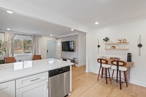 A modern kitchen with a dishwasher, a dining area with bar stools, and a TV mounted on the wall. - Luxury Stay with Hot Tub, Fire Pit and Games (Charlotte)
