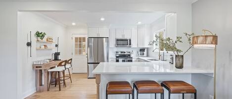 A modern kitchen with white cabinetry, stainless steel appliances, and a central island with stools.