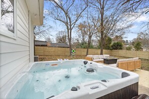 Ein Whirlpool mit Warnhinweis, umgeben von Gartenmöbeln und einem Holzzaun.