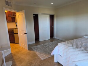 Ein Schlafzimmer mit einem Bett, einer weißen Tür zu einem Schrank und einem durch eine offene Tür einsehbaren Küchenbereich.
