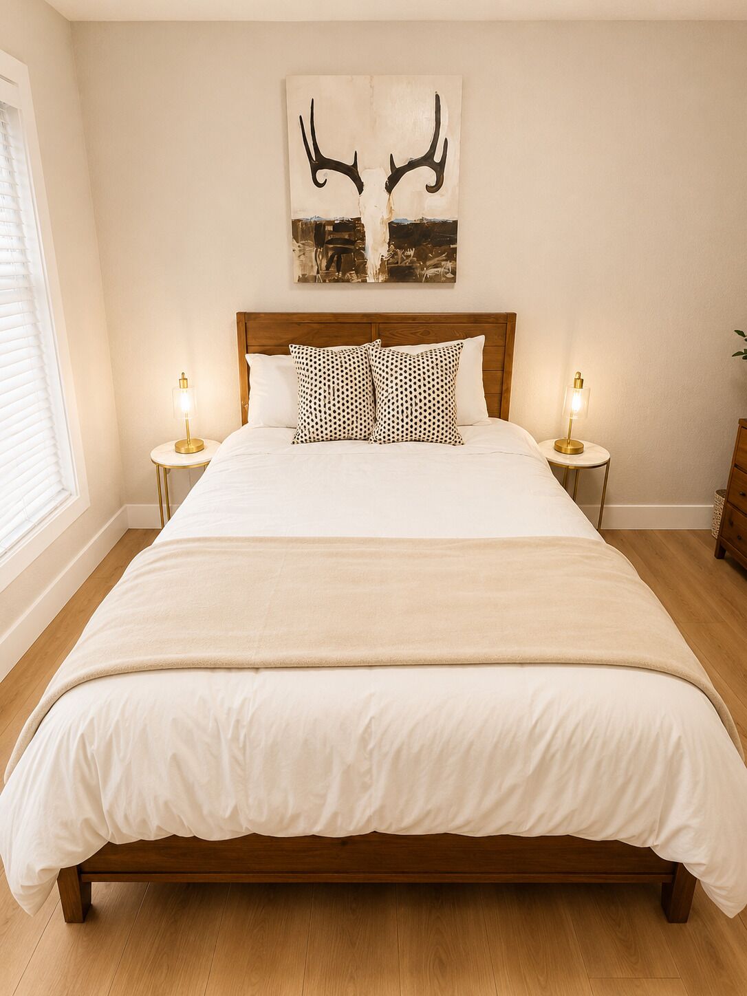 Un dormitorio con una cama grande, dos mesitas de noche con lámparas, un cabecero de madera y una obra de arte con motivos de astas colgada en la pared.