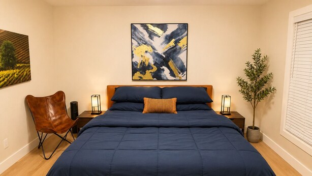 Une chambre à coucher avec un grand lit, une chaise, une plante en pot et des œuvres d’art accrochées au mur.
