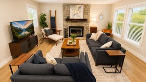 Un salon avec une cheminée, un téléviseur et un ensemble de meubles (canapé, fauteuils, etc.).
