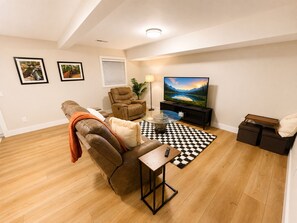 A living room with a brown leather sofa, a glass coffee table, a black and white checkered rug, a television, and framed pictures on the wall. - Lakefront w/ boat dock, close to MTB trails and OZ Bike park and lift! (Bella Vista)