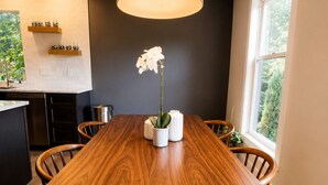 Un espace repas moderne avec une table en bois, des chaises, un luminaire suspendu et une fenêtre laissant entrer la lumière naturelle.
