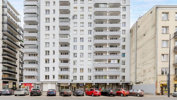 A multi-story residential building with balconies, a ground-level commercial area with shops, and parked cars. - City Apartment in Warsaw (Warsaw)