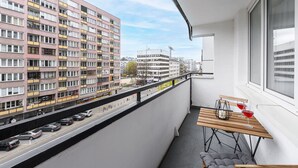 A balcony with a view of a multi-story building, a table with a bottle and glasses, and a bench. - City Apartment in Warsaw (Warsaw)