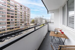 Ein Balkon mit Blick auf ein mehrstöckiges Gebäude, ein Tisch mit einer Flasche und Gläsern sowie eine Bank.