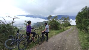 Dos personas en un sendero de tierra con bicicletas, rodeadas de vegetación y montañas al fondo.