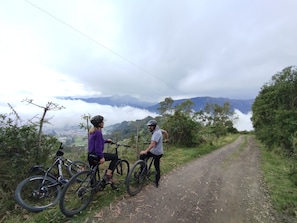 Two people on a dirt path with bicycles, surrounded by greenery and mountains in the background. - Casa Pájaro Azul (Isinlivi)