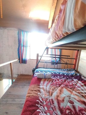 A bunk bed with a patterned blanket, a window with curtains, and a wooden floor.
