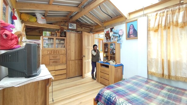 Una habitación compacta con cama, muebles de madera, televisión y ventana con cortinas.