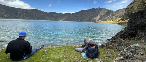Two people sitting by a lake with mountains in the background.