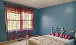 A bedroom with a single bed, a window with patterned curtains, and a blue wall.