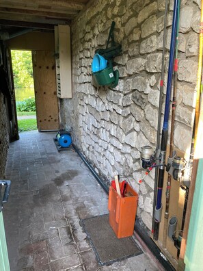 A stone-walled corridor with a wooden door leading outside, a blue water container, and a red toolbox. - L'ÉCRIN DES BORDS DE SEINE: A vacation rental nestled in the heart of Normandy on the banks of the Seine. (Poses)