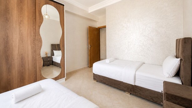 Quarto de hotel com duas camas, um guarda-roupa de madeira, um espelho e uma luminária suspensa.