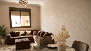 Uma sala de jantar com uma mesa posta para quatro pessoas, um sofá marrom e um vaso de plantas.