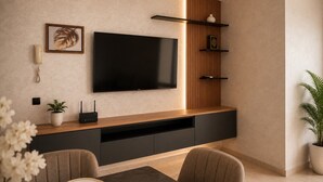 Uma sala de estar moderna com televisão de tela plana fixada em uma parede de painéis de madeira, um rack de entretenimento embutido abaixo e uma área de jantar com mesa e cadeiras.