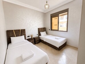 A hotel room with two beds, a window, and a nightstand with a vase. - Modern and Cozy (Agadir)