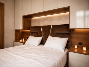 Une chambre à coucher moderne avec un grand lit, deux tables de chevet ornées de bougies et une tête de lit en bois.