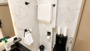 Casa de banho moderna com painel de fundo de mármore, sanita preta, lavatório com dispensador de sabão e suporte de toalhas.